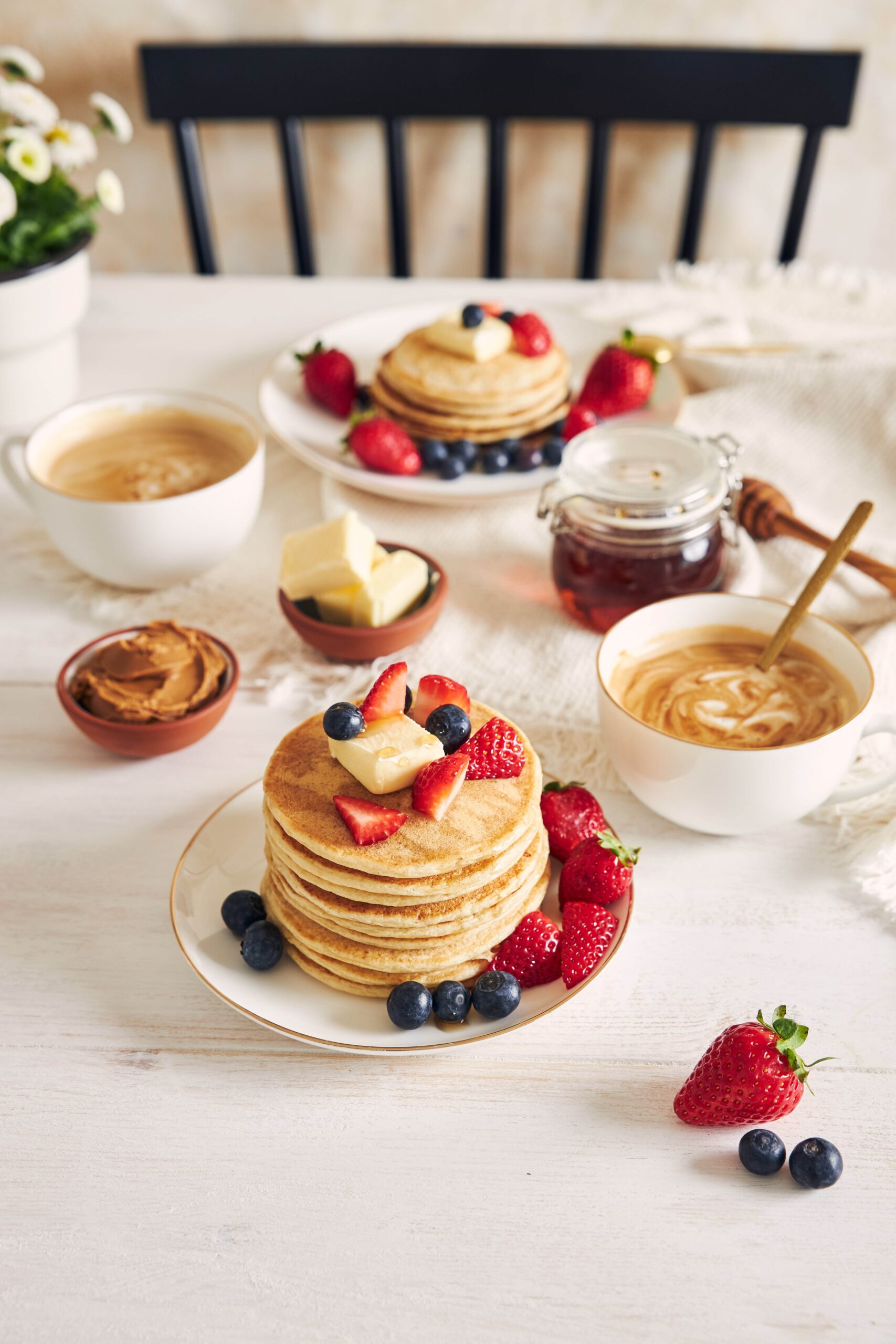 A vertical shot of Delicious vegan Tofu Pancakes with colorful Fruits, Syrup  and Coffee on a white wood Table